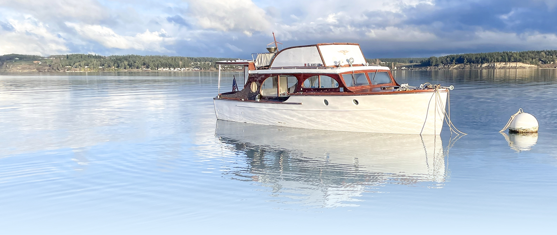 Center for Electric Marine Innovation. Gorgeous white and teak wooden boat tied to a montage buoy at sunrise on a calm morning with a blurred reflection and a cloudy backdrop. A Non Profit.