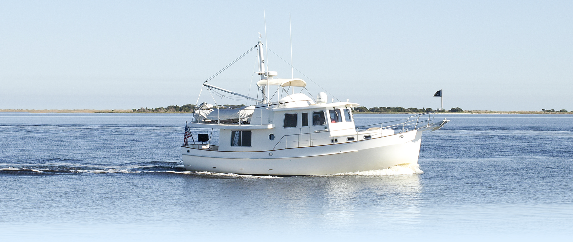 Gorgeous white and teak wooden boat tied to a montage buoy at sunrise on a calm morning with a blurred reflection and a cloudy backdrop.